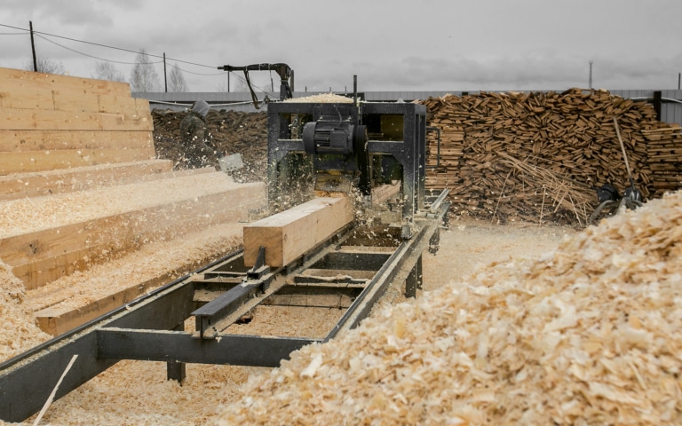 Am Gelände eines Sägewerks wird ein Holzbalken maschinell bearbeitet